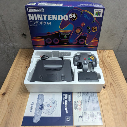 Opened Nintendo 64 boxed console set on wooden table with styrofoam tray controller cables and Japanese manual