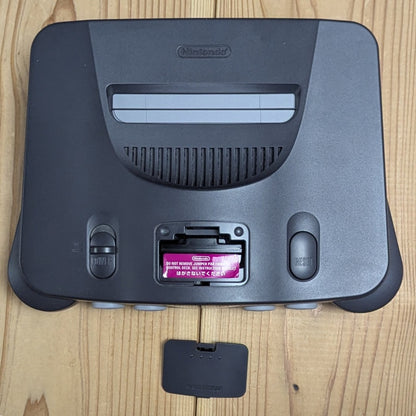 Top view of N64 Charcoal Grey console showing expansion bay door open with authentic purple Jumper Pak installed