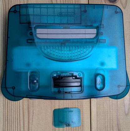 Top view of N64 Clear Blue console with expansion bay cover open displaying authentic Jumper Pak installed